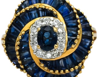 May include: A gold ring featuring a central oval-cut, dark blue gemstone surrounded by a halo of small white diamonds. The ring's design includes a spiral of baguette-cut, deep blue gemstones, creating a striking contrast. The ring is a piece of jewelry.