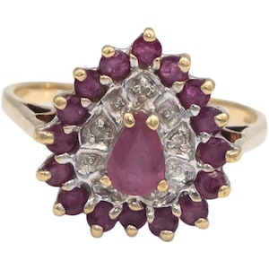 Peut inclure: Bague en or ornée d'un groupe de pierres précieuses rouge foncé entourant un rubis central en forme de goutte. La bague présente un design en halo avec de petites pierres et des accents dorés, d'aspect vintage.