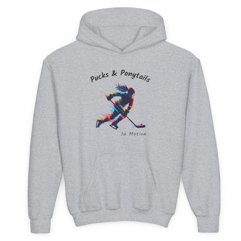 Puede incluir: Una sudadera con capucha gris claro con el texto "Pucks & Ponytails" y una ilustraci&oacute;n de un jugador de hockey en movimiento. La ilustraci&oacute;n presenta un dise&ntilde;o colorido y estilizado de una persona con una cola de caballo jugando al hockey.
