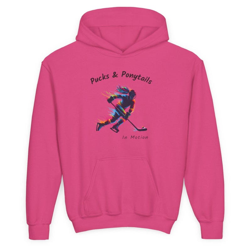 Puede incluir: Una sudadera con capucha rosa intenso con un bolsillo delantero y una capucha. La sudadera presenta el texto "Pucks & Ponytails" sobre una colorida ilustraci&oacute;n de una jugadora de hockey en movimiento. Debajo de la ilustraci&oacute;n est&aacute; el texto "In Motion."