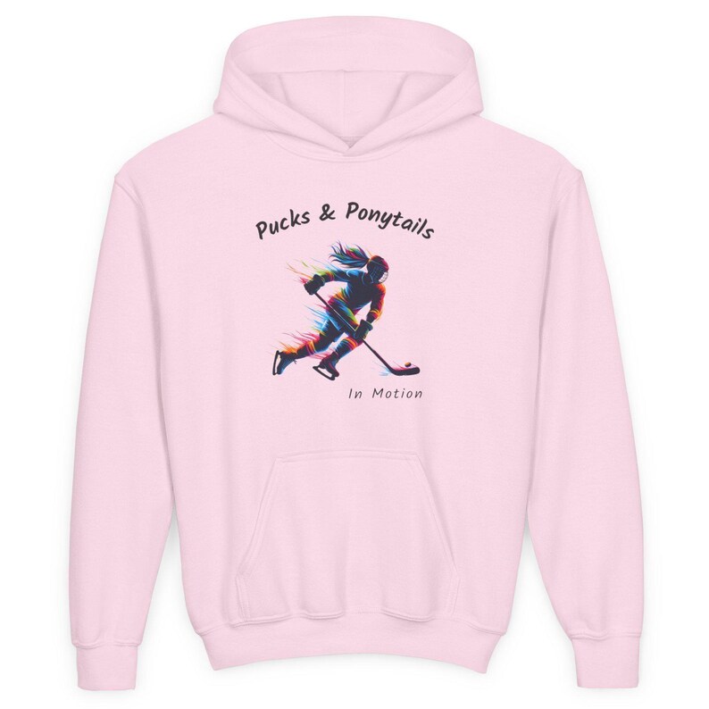 Puede incluir: Sudadera con capucha rosa claro con bolsillo delantero y capucha. El gr&aacute;fico frontal presenta a una jugadora de hockey en movimiento con el texto "Pucks & Ponytails In Motion". El dise&ntilde;o utiliza un efecto colorido y estilizado.