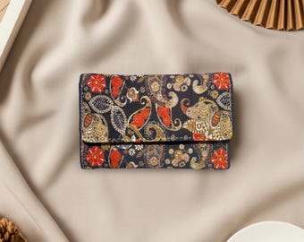 May include: A small, rectangular wallet with a dark background and a colorful paisley pattern. The pattern includes red, gold, and white floral and swirl designs. The wallet has a navy blue border and a fold-over flap.