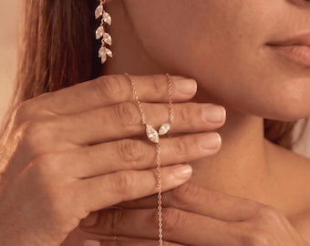 May include: A gold-toned jewelry set consisting of a drop earring and a lariat necklace. The earring features a vertical row of marquise-cut clear stones in a leaf-like arrangement. The necklace has a central Y-shaped drop with clear stones.