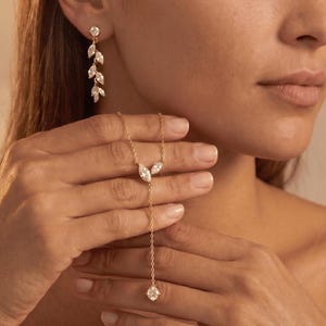 May include: A gold-toned jewelry set consisting of a lariat-style necklace and drop earrings. The necklace features a delicate chain with two marquise-cut clear stones and a single round stone drop. The earrings feature a vertical vine-like design.