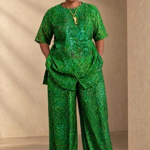 May include: A two-piece outfit consisting of a short-sleeved, round-neck top and matching wide-leg trousers. The set is crafted from a vibrant green fabric featuring a detailed, tonal botanical leaf pattern throughout the entire garment.