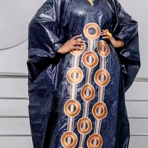 May include: A navy blue, long-sleeved dress with a matching head wrap. The dress features a pattern of large, copper-colored circles with white and copper accents. The fabric has a subtle, textured appearance. The dress has a V-neck and a loose, flowing fit.
