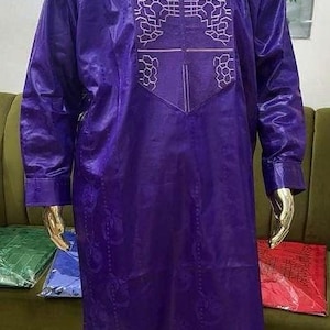 May include: A purple two-piece outfit on a gold mannequin. The long-sleeved tunic features an embroidered design on the chest. The matching pants complete the ensemble. The outfit is displayed on a mannequin with a gold head and hands.