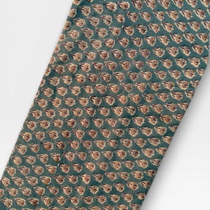 A long, narrow strip of teal blue fabric with a repeating pattern of light brown and white floral motifs is laid diagonally across a white background.