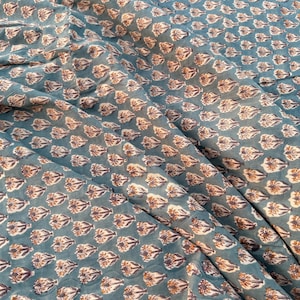 A teal blue cotton fabric with light brown and white floral motifs, draped with soft folds and shadows.