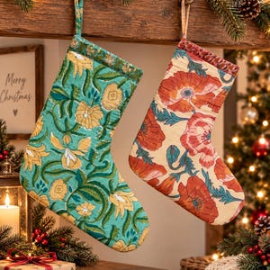 May include: Two fabric Christmas stockings hanging from a wooden mantel. The left stocking features a teal background with yellow floral patterns. The right stocking has a cream background with large red poppy flowers and green foliage designs.