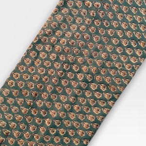 A long, narrow strip of teal blue fabric with a repeating pattern of light brown and white floral motifs is laid diagonally across a white background.