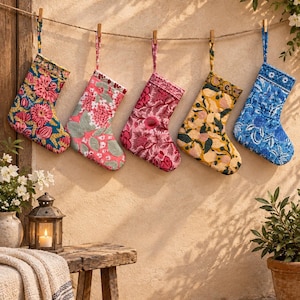 May include: Five quilted fabric stockings hanging from a rope with wooden clips. The stockings feature various floral patterns in vibrant colors including blue, yellow, pink, and red. Each stocking has a loop at the top for hanging purposes.