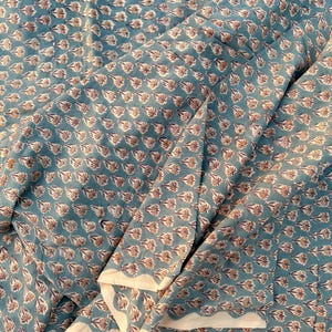 A teal blue cotton fabric with light brown and white floral motifs, draped with several soft folds and a visible white edge.