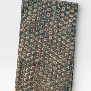 A long, folded piece of teal blue fabric with light brown and white floral motifs is displayed vertically on a white background, showing a light-colored border.