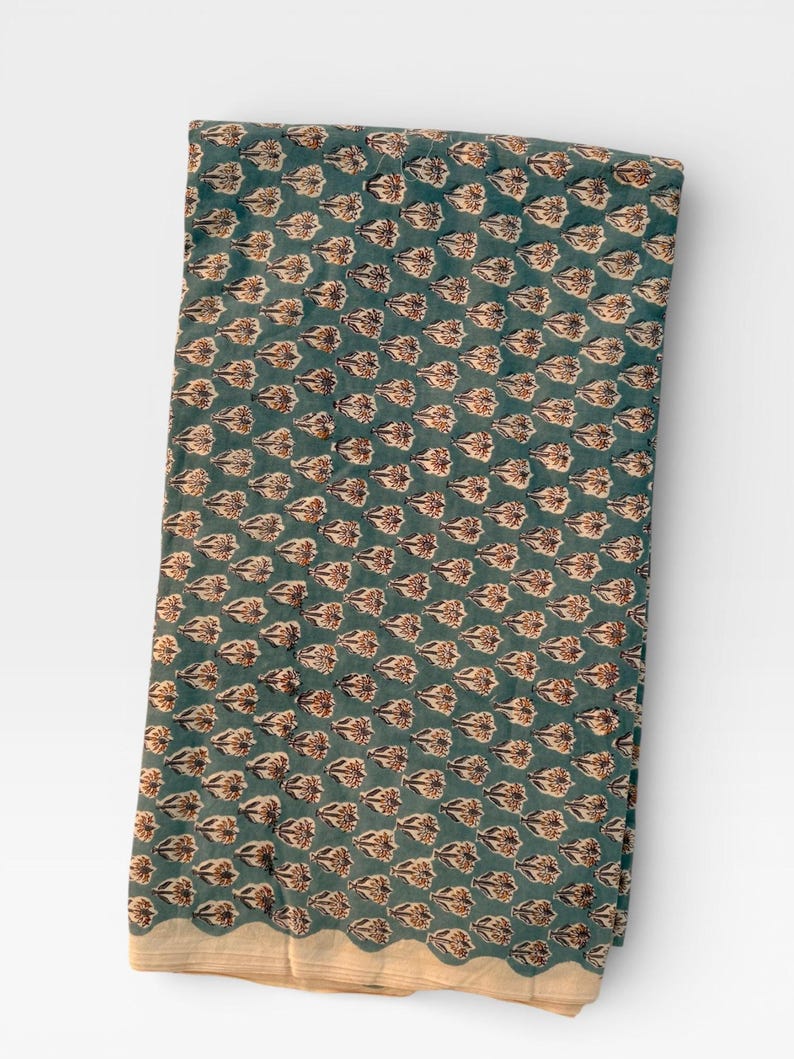 A long, folded piece of teal blue fabric with light brown and white floral motifs is displayed vertically on a white background, showing a light-colored border.