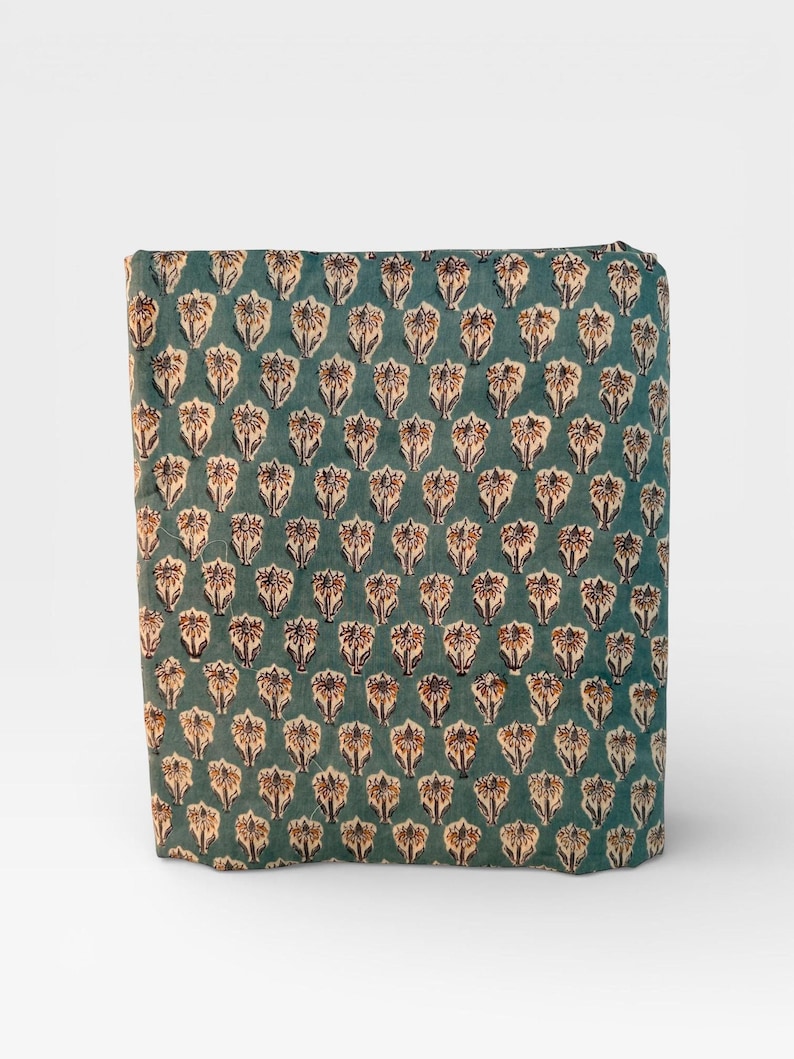 A rectangular block of teal blue fabric with a repeating pattern of light brown and white floral motifs is standing upright on a white background.