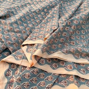 A teal blue cotton fabric with light brown and white floral motifs, folded into multiple layers, revealing a light tan underside.