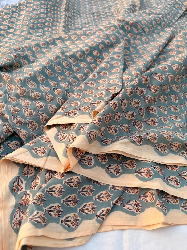 A teal blue cotton fabric with light brown and white floral motifs, folded into multiple layers, revealing a light tan underside.