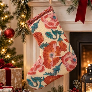 Puede incluir: Un calcetín navideño con una base de tela color crema y un patrón floral repetitivo de grandes amapolas naranjas y rosas con hojas y tallos verde azulado. El puño superior tiene un borde decorativo fino y una pequeña presilla de tela.