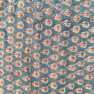 A close-up, slightly blurry view of a light blue fabric with a repeating pattern of white, orange, and purple floral motifs.