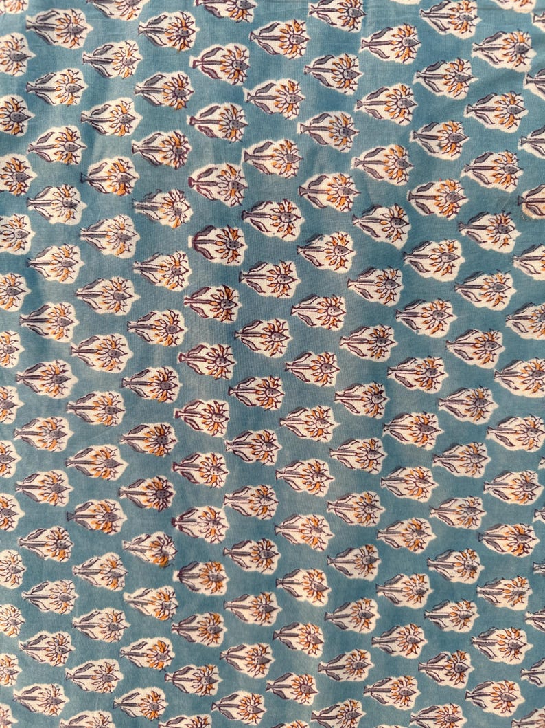 A close-up, slightly blurry view of a light blue fabric with a repeating pattern of white, orange, and purple floral motifs.