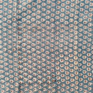 A flat, teal blue cotton fabric with a repeating pattern of small, light brown and white floral motifs.