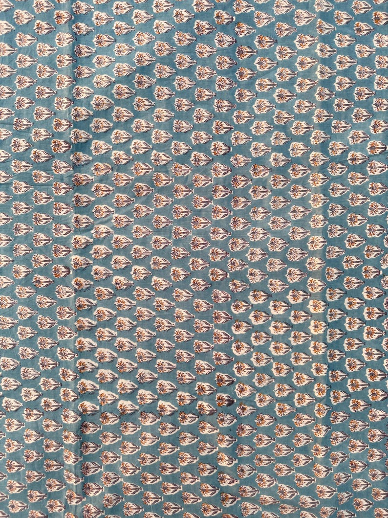 A flat, teal blue cotton fabric with a repeating pattern of small, light brown and white floral motifs.