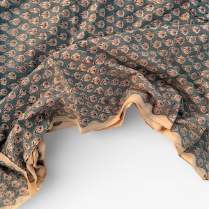 A teal blue cotton fabric with light brown and white floral motifs, draped over a white surface, revealing a light tan underside.