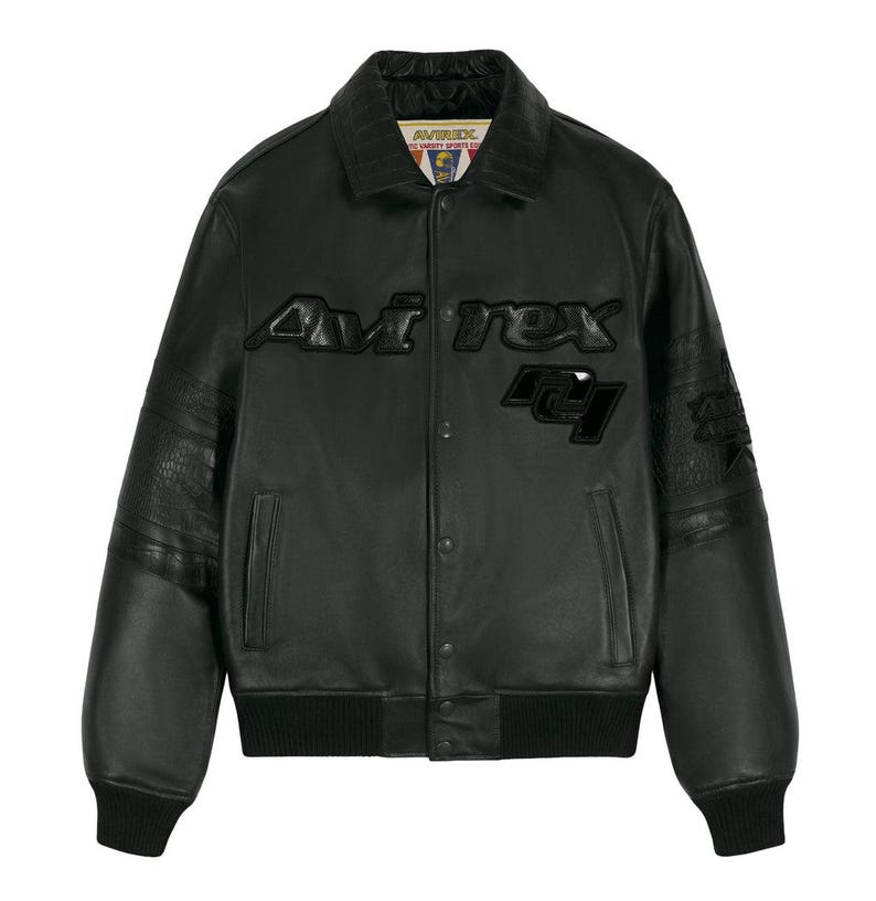 May include: A black leather varsity jacket featuring a fold-down collar, snap-button front closure, and ribbed cuffs and hem. The chest displays the text 'Avirex' in raised black lettering, with a matching black graphic patch below the text.
