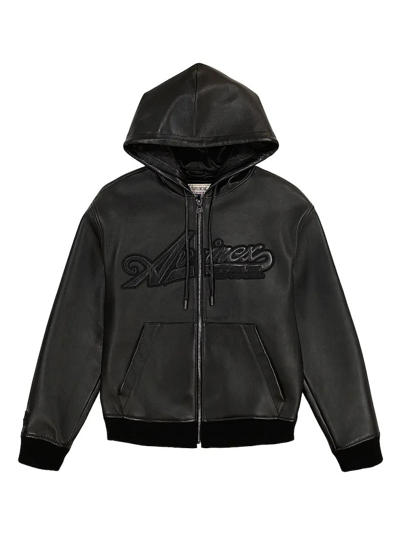 May include: Black leather zip-up hoodie with a drawstring hood and a black ribbed hem and cuffs. The word "Aviirex" is embroidered across the chest in a stylized font. The jacket has two front pockets.