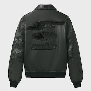 May include: A black leather jacket featuring a classic collar, ribbed cuffs, and a ribbed hem. The back displays embossed black lettering that reads All Star and Coolers, along with a central geometric graphic. The sleeves have textured panels.