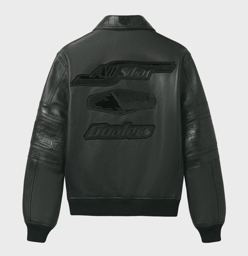 May include: A black leather jacket featuring a classic collar, ribbed cuffs, and a ribbed hem. The back displays embossed black lettering that reads All Star and Coolers, along with a central geometric graphic. The sleeves have textured panels.