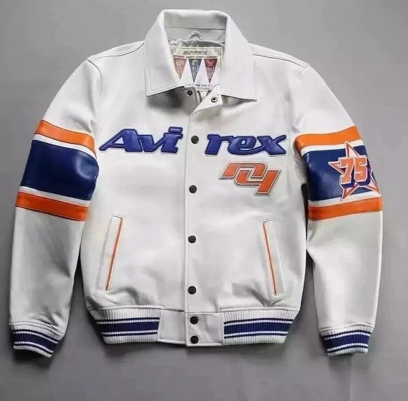 Puede incluir: Chaqueta de cuero blanca con detalles en azul y naranja. Presenta el texto "Avirex" en azul y el n&uacute;mero "75" en la manga. La chaqueta tiene un estilo bomber cl&aacute;sico con cierre de botones y pu&ntilde;os a rayas.