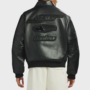 May include: A black leather bomber jacket featuring a ribbed collar, cuffs, and hem. The back displays embossed black patches with the text "ALL STAR" and "Qualers" in a stylized font, along with textured crocodile-patterned leather sleeves.