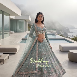 May include: A sage green lehenga choli set featuring intricate silver embroidery, beadwork, and a scalloped hemline on the bodice. The skirt displays detailed floral patterns and geometric motifs. Text on the image reads Wedding Dress 2026.