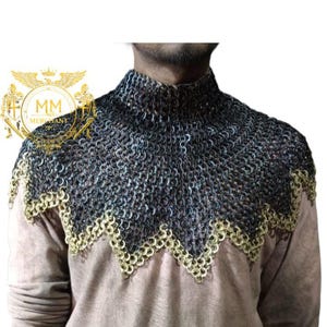 May include: A chainmail coif, a medieval neck and shoulder defense, is displayed. The coif is made of interlocking metal rings in shades of silver and black, with a decorative gold-colored edge. The coif is worn over a light brown garment.