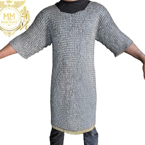 May include: A silver chainmail shirt with short sleeves. The shirt is made of small, interlocking metal rings. The bottom hem has a gold-colored trim. The shirt is designed to be worn as protective armor.