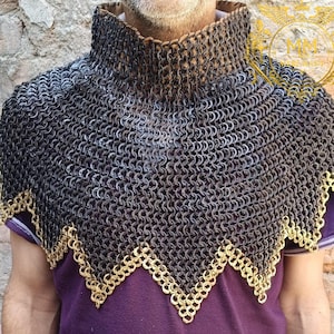 May include: A chainmail coif with a high collar and a decorative gold-colored trim along the bottom edge. The chainmail is made of small, interlocking metal rings. The coif is worn over a purple shirt.