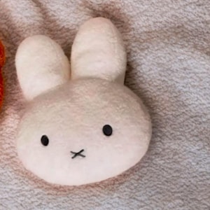 May include: A plush white bunny toy with black eyes and a black 'X' for a mouth. The bunny has large, upright ears and a soft, textured appearance. The toy is likely designed for children.