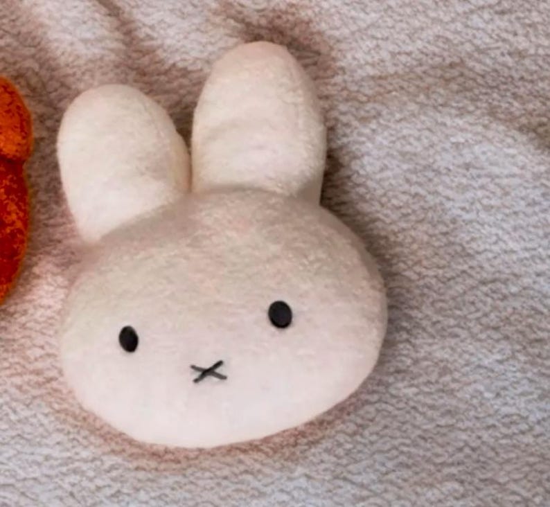 May include: A plush white bunny toy with black eyes and a black 'X' for a mouth. The bunny has large, upright ears and a soft, textured appearance. The toy is likely designed for children.