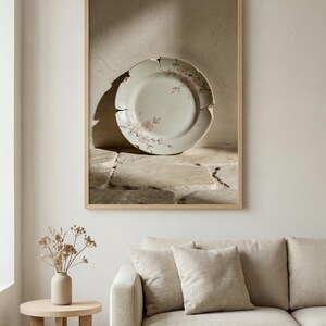 May include: A framed image of a cracked, antique plate with a floral design. The plate is light green with pink flowers and sits on a stone surface. The frame is light wood, and the overall aesthetic is vintage.