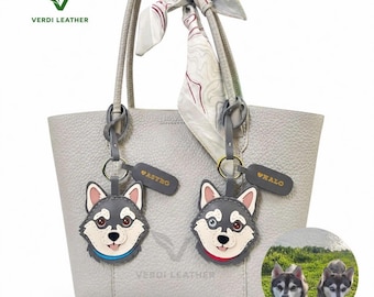 May include: A light gray pebbled leather tote bag featuring two custom dog-shaped charms labeled ASTRO and HALO, a patterned silk scarf tied to the handle, and a circular inset showing two husky dogs in a grassy field.