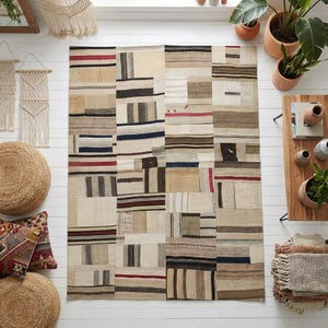 May include: A rectangular patchwork rug with a neutral color palette. The rug features a variety of rectangular and square patches in shades of beige, brown, and gray, with accents of red, blue, and black. The rug is a floor covering.