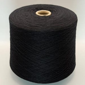 May include: A large cylindrical spool of solid black yarn. The thread is tightly wound in a crisscross pattern around a central cardboard core, creating a uniform and dense texture throughout the entire surface of the spool.