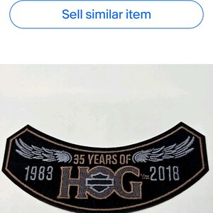 May include: Black and brown embroidered patch with the text "35 YEARS OF HOG 1983-2018". The patch has a curved shape with wings on each side. Motorcycle-themed apparel.