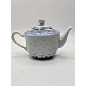 May include: White porcelain teapot with a blue patterned design around the lid and base. The teapot has a curved handle and a spout. The body of the teapot is decorated with small, evenly spaced blue dots.