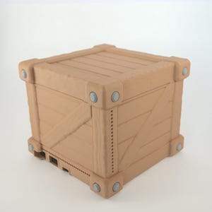 May include: A light brown, cube-shaped storage container designed to resemble a wooden shipping crate. The exterior features horizontal slats, diagonal bracing, and reinforced corners with circular gray accents. The base includes ventilation slots.