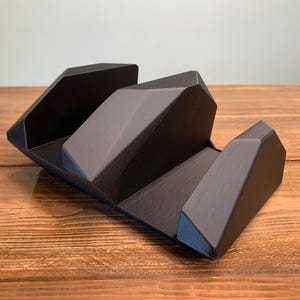 May include: A black, geometric desk organizer with a faceted design. The organizer has three sections and is made of a matte material. It sits on a wooden surface.
