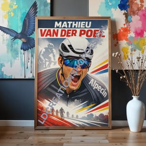 Puede incluir: Póster enmarcado del ciclista Mathieu van der Poel, con el texto "Mathieu Van Der Poel" en rojo y blanco. El póster tiene un marco de madera y se exhibe sobre un suelo de madera. El ciclista lleva casco y gafas de sol.