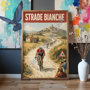 May include: A framed print of a cycling race titled "Strade Bianche." The artwork depicts cyclists on a dusty road winding through the Italian countryside. A cyclist in a red jersey is in the foreground, with other cyclists in the distance.